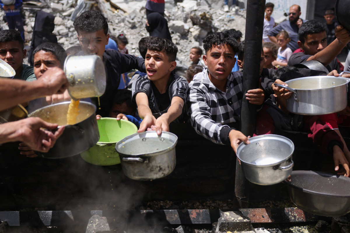 Palestinos deslocados se reúnem para coletar porções de alimentos cozidos em uma distribuição de caridade em Jabalia, no norte da Faixa de Gaza