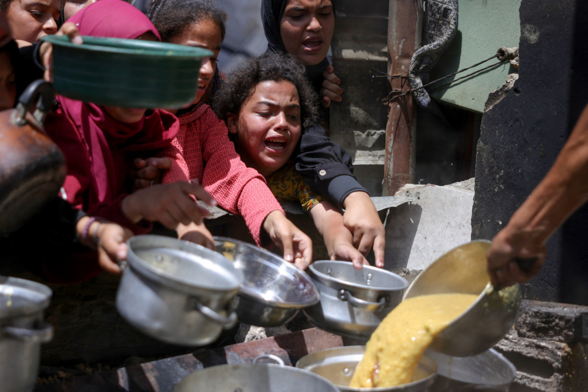 Palestinos deslocados se reúnem para coletar porções de alimentos cozidos em uma distribuição de caridade em Jabalia, no norte da Faixa de Gaza