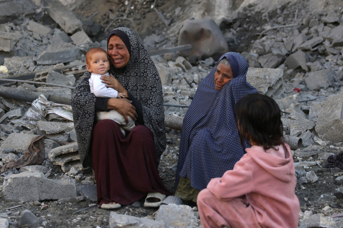 Mulher segurando um bebê chora enquanto palestinos verificam o local de um ataque israelense durante a noite