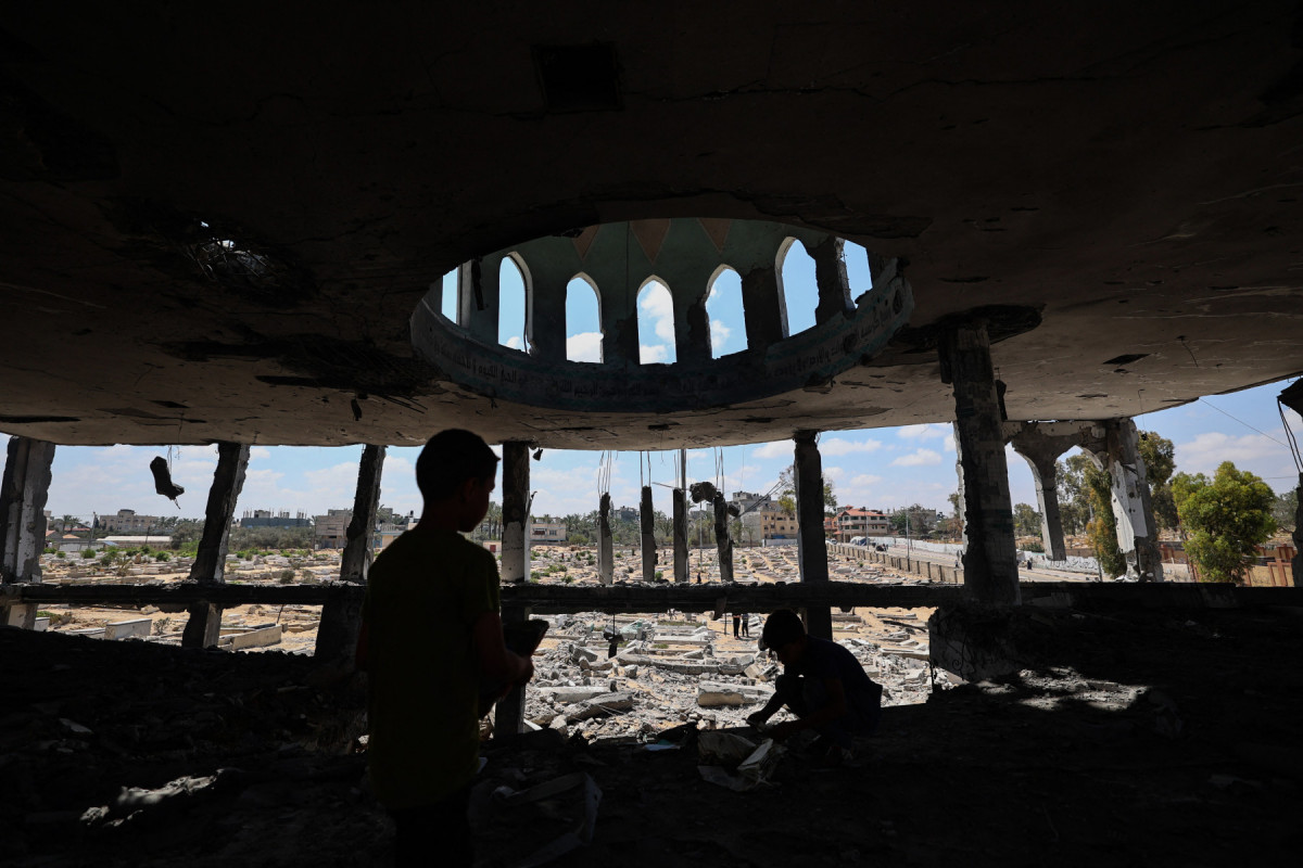 
Crianças palestinas recuperam livros danificados após um ataque israelense que atingiu a Mesquita Ansar e um cemitério adjacente em Deir el-Balah, no centro da Faixa de Gaza, em 3 de junho de 2025. (Foto de Eyad BABA / AFP)