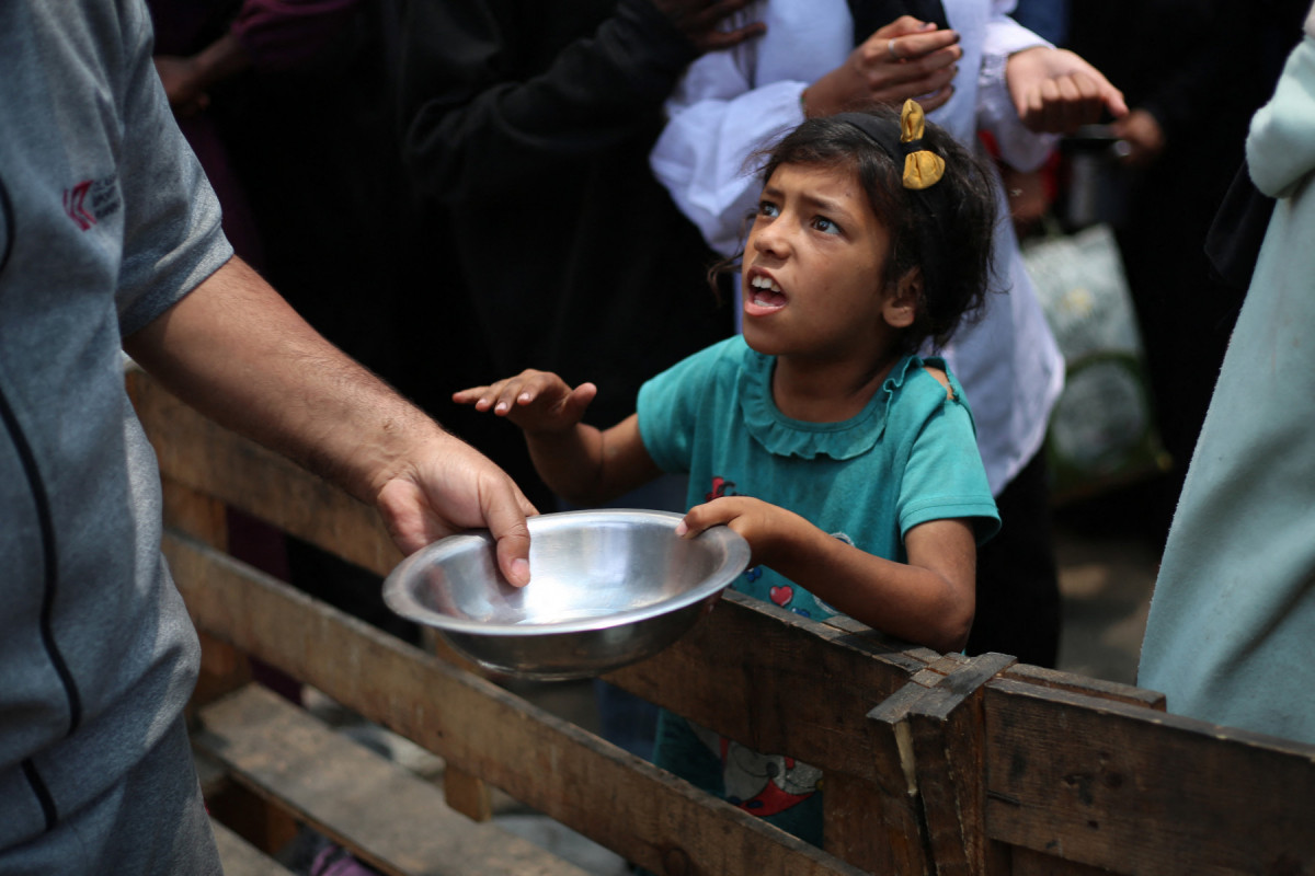 Uma menina palestina segura uma panela vazia em um ponto de distribuição de refeições quentes em Nuseirat, no centro da Faixa de Gaza