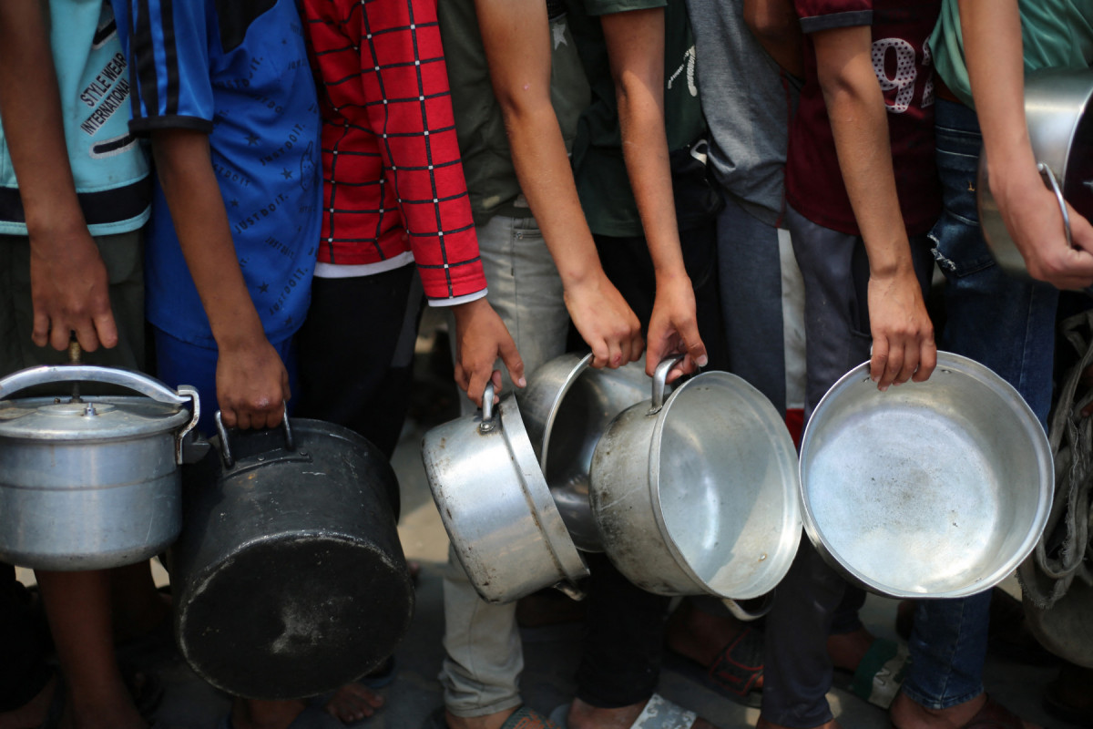 Meninos palestinos carregam panelas enquanto fazem fila em um ponto de distribuição de refeições quentes em Nuseirat, no centro da Faixa de Gaza (Eyad BABA/AFP) Meninos palestinos carregam panelas enquanto fazem fila em um ponto de distribuição de refeições quentes em Nuseirat, no centro da Faixa de Gaza/Eyad BABA/AFP
