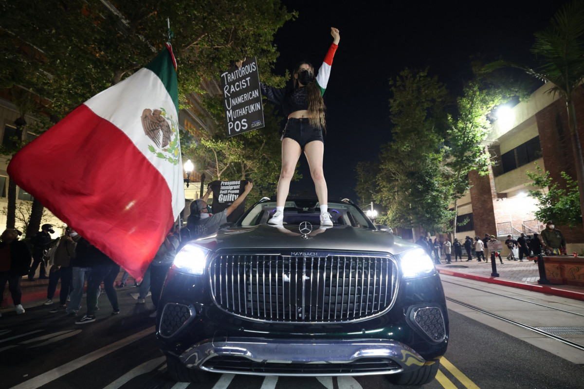 Mulher em cima de um carro com uma bandeira mexicana e um cartaz enquanto manifestantes se reúnem perto do Edifício Federal em Santa Ana, Califórnia (Patrick T. Fallon/AFP) Mulher em cima de um carro com uma bandeira mexicana e um cartaz enquanto manifestantes se reúnem perto do Edifício Federal em Santa Ana, Califórnia/Patrick T. Fallon/AFP
