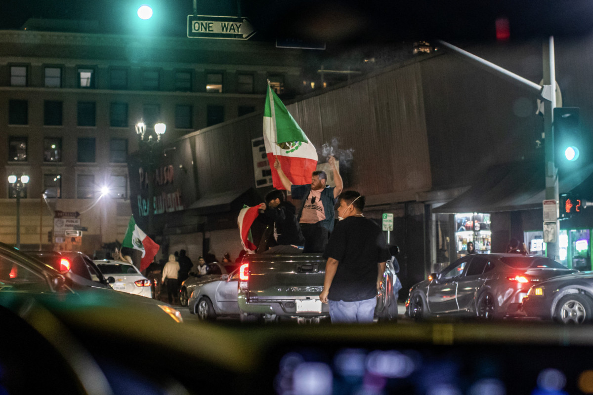 Manifestantes com bandeiras do México andam de caminhonete em uma rua no centro da cidade após o toque de recolher ter sido imposto após dias de protestos em resposta às operações federais de imigração em Los Angeles, em 10 de junho de 2025. A polícia de Los Angeles começou a prender pessoas no centro da cidade na noite de 10 de junho, enquanto grupos se reuniam em violação ao toque de recolher noturno após o quinto dia de protestos contra a repressão imigratória de Donald Trump. (Foto de Apu GOMES / AFP)