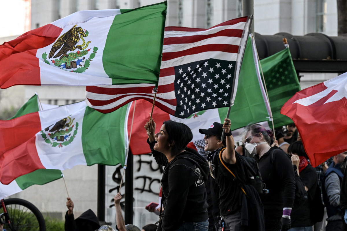 Pessoas agitam bandeiras mexicanas, americanas e uma bandeira americana de cabeça para baixo enquanto protestam contra as operações federais de imigração perto da Prefeitura de Los Angeles, em 11 de junho de 2025. Protestos contra as duras políticas de imigração de Donald Trump se espalharam pelos Estados Unidos em 11 de junho, apesar da repressão apoiada pelos militares em Los Angeles e das ameaças do presidente republicano de extrema direita de usar 