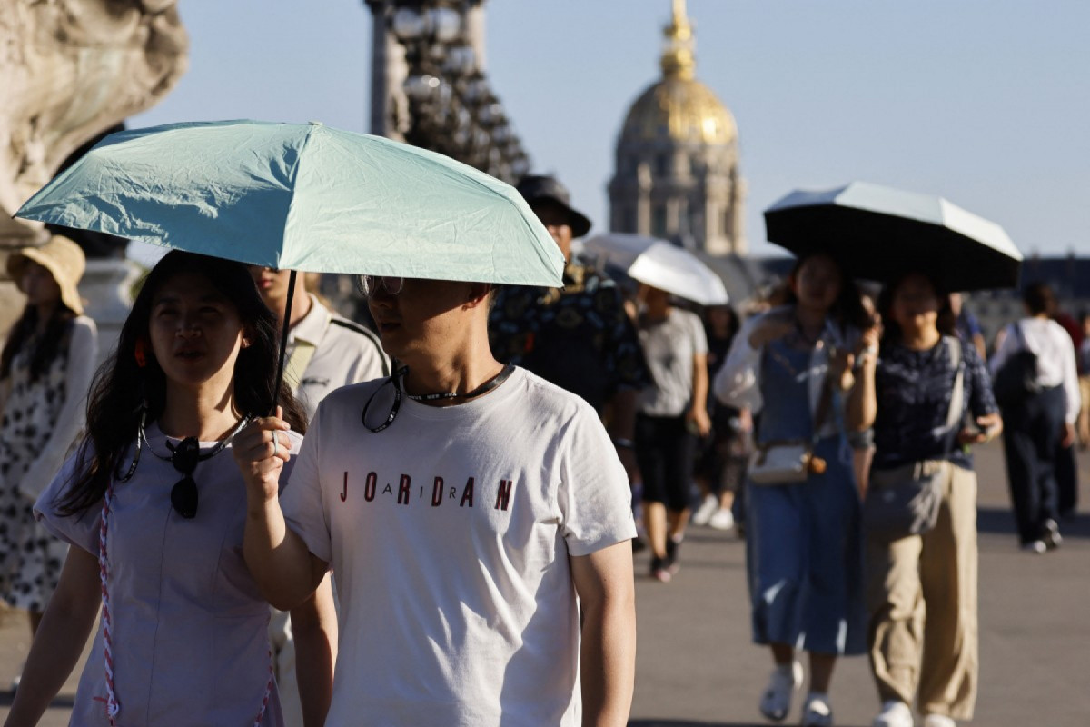 Turistas seguram guarda-chuvas para se proteger do sol durante uma onda de calor em Paris, em 30 de junho de 2025. As autoridades francesas colocaram Paris em alerta vermelho devido ao calor extremo, e Espanha e Portugal registraram temperaturas recordes enquanto uma onda de calor assolava o sul da Europa e a Grã-Bretanha em 30 de junho de 2025, disparando alertas de saúde e alimentando incêndios florestais. (Foto de Ludovic MARIN / AFP)