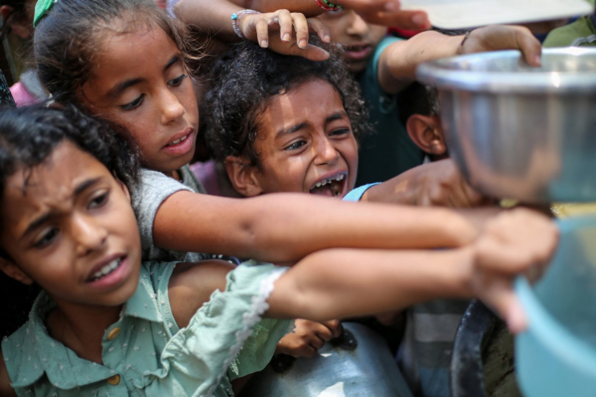 Crianças palestinas fazem fila para receber uma refeição quente em um ponto de distribuição de alimentos em Nuseirat, em 30 de junho de 2025. Após mais de 20 meses de conflito devastador entre Israel e o movimento militante islâmico Hamas, grupos de direitos humanos afirmam que a população de Gaza, de mais de dois milhões de pessoas, enfrenta condições semelhantes à fome. (Foto de Eyad BABA / AFP)