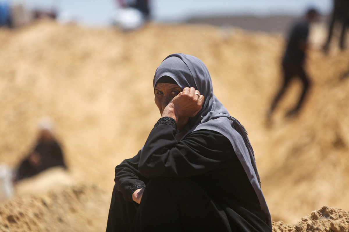 Uma mulher observa palestinos inspecionarem tendas destruídas em um campo improvisado para deslocados após uma suposta incursão de tanques israelenses na área de Khan Yunis, no sul da Faixa de Gaza, em 11 de julho de 2025. (Foto da AFP)
