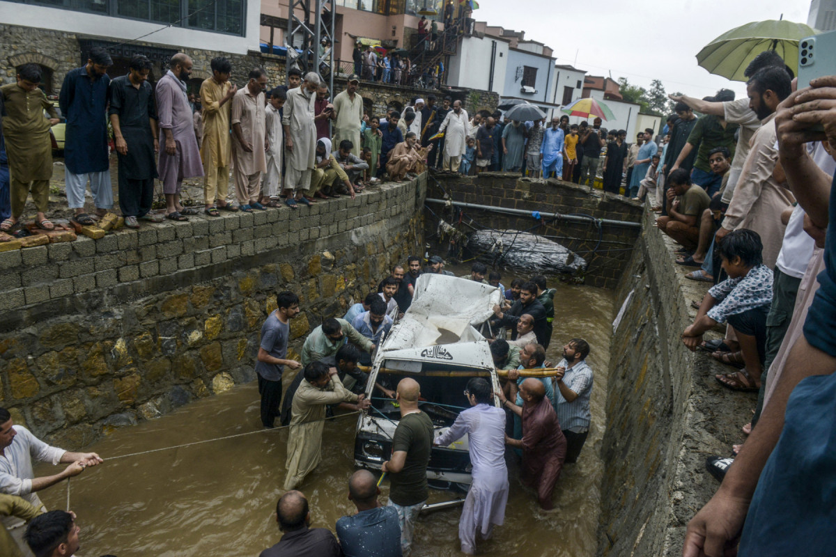 Pessoas removem os destroços de uma van de um bueiro após fortes chuvas de monções em Islamabad, em 21 de julho de 2025. (Foto de M ASIM KHAN / AFP)