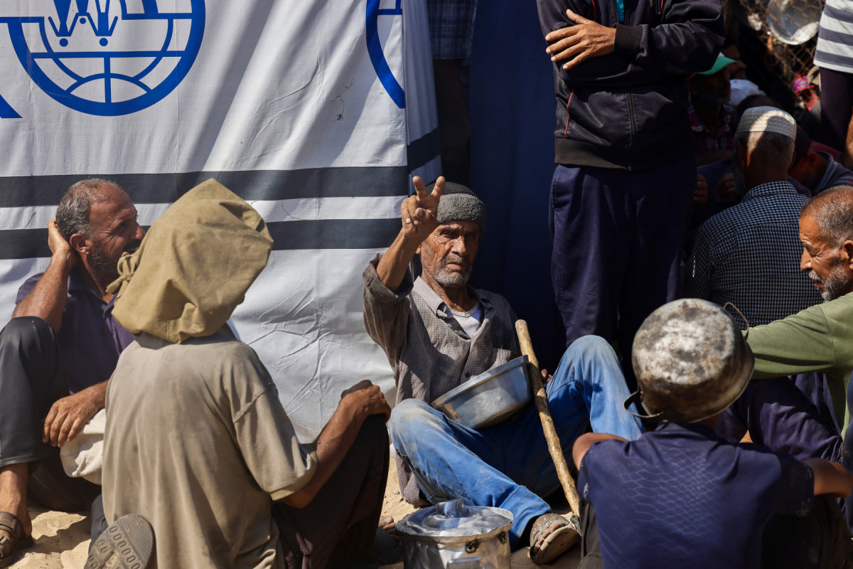 Um idoso palestino faz o sinal da vitória enquanto espera para receber uma refeição quente em uma cozinha beneficente na área de Mawasi, em Khan Yunis, no sul da Faixa de Gaza, em 22 de julho de 2025. O chefe do maior hospital de Gaza disse que 21 crianças morreram de desnutrição e fome no território palestino nos últimos três dias, em meio a um ataque devastador das forças israelenses. (Foto da AFP)
