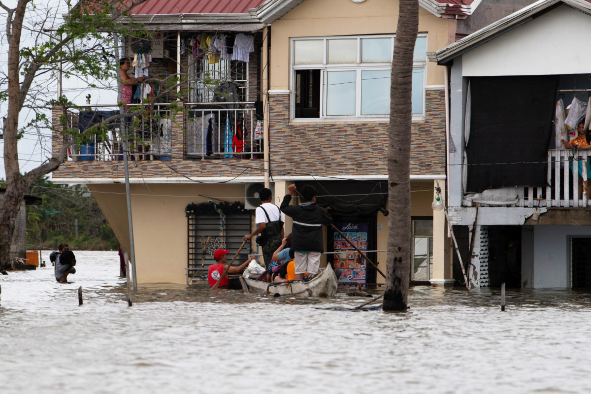 Moradores a bordo de um barco de madeira atracam em sua casa submersa em um vilarejo na cidade de Calumpit, província de Bulacan, ao norte de Manila, em 25 de julho de 2025, após o transbordamento de um rio devido às fortes chuvas causadas pelo Tufão Co-May. Equipes de resgate no norte das Filipinas resgataram moradores isolados pelas enchentes e entregaram suprimentos de barco em 25 de julho, após o Tufão Co-May ter sido rebaixado para tempestade tropical horas após atingir a costa oeste. (Foto de Ted ALJIBE / AFP)