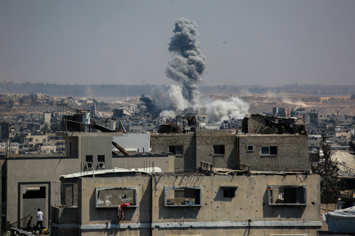 Dois palestinos no telhado de um prédio enquanto a fumaça sobe após os ataques israelenses em Jabalia, no norte da Faixa de Gaza, em 13 de julho de 2025. Delegações de Israel e do grupo militante palestino Hamas já passaram uma semana tentando chegar a um acordo sobre uma trégua temporária para interromper 21 meses de combates devastadores na Faixa de Gaza. (Foto de Bashar TALEB / AFP)