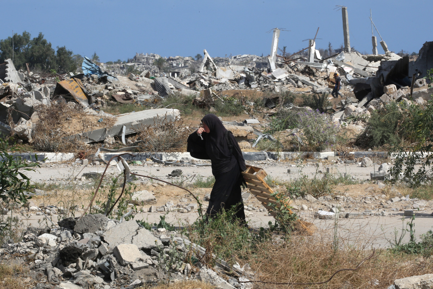 Uma mulher palestina deslocada bebe água enquanto transporta um pedaço de madeira no centro da Faixa de Gaza, em 30 de julho de 2025. Alertas de fome na Faixa de Gaza aumentaram após quase 22 meses de guerra, com o número de mortos aumentando e sem sinais de um avanço iminente nas negociações de trégua. (Foto de Eyad BABA / AFP)
