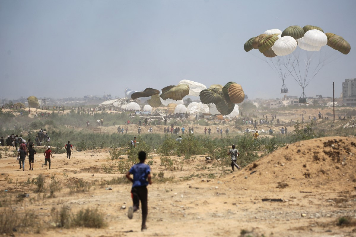 Palestinos correm para o local onde pacotes de ajuda humanitária lançados de paraquedas estão pousando na área de Nuseirat, no centro da Faixa de Gaza, durante um lançamento aéreo sobre o território palestino sitiado por Israel em 6 de agosto de 2025. (Foto de Eyad BABA / AFP)/ AFP
