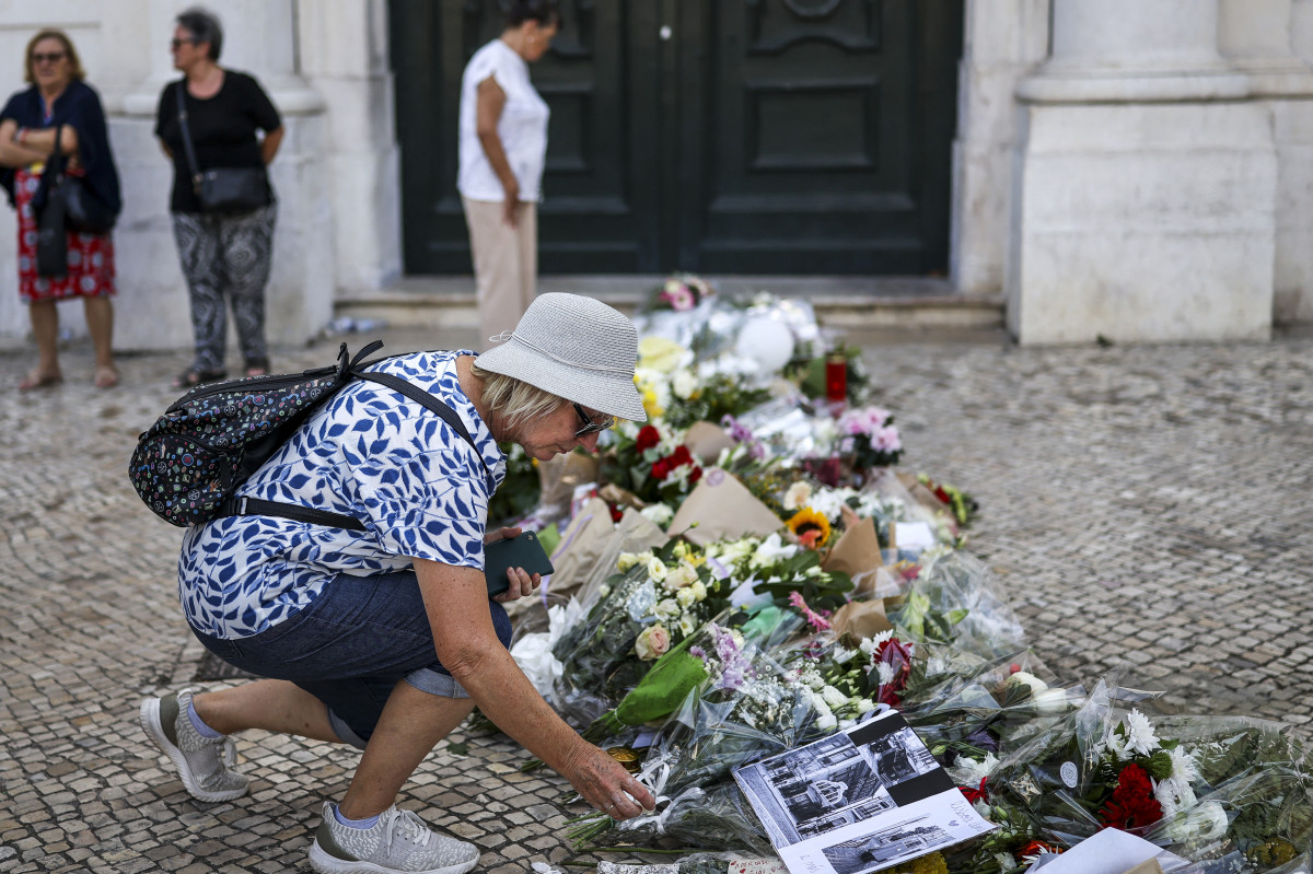 Pessoas posam ao lado de flores em homenagem às vítimas do acidente do funicular da Glória, em Lisboa (PATRICIA DE MELO MOREIRA / AFP) Pessoas posam ao lado de flores em homenagem às vítimas do acidente do funicular da Glória, em Lisboa/PATRICIA DE MELO MOREIRA / AFP