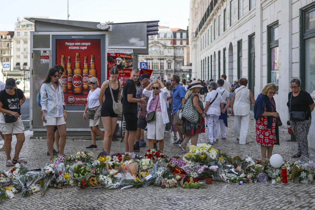 Pessoas posam ao lado de flores em homenagem às vítimas do acidente do funicular da Glória, em Lisboa (PATRICIA DE MELO MOREIRA / AFP) Pessoas posam ao lado de flores em homenagem às vítimas do acidente do funicular da Glória, em Lisboa/PATRICIA DE MELO MOREIRA / AFP
