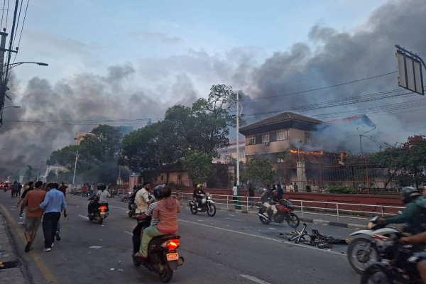 Commuters ride past the burning Supreme Court building, set ablaze by protesters in Kathmandu on September 9, 2025, a day after a police crackdown on demonstrations over social media prohibitions and corruption by the government. Nepal's president called for national unity on September 9, after two days of violent protests, including rallies against a government ban on social media that forced the prime minister to resign and left at least 19 people dead.