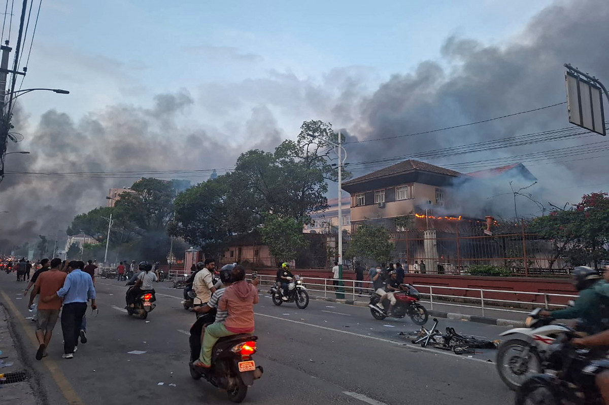  Commuters ride past the burning Supreme Court building, set ablaze by protesters in Kathmandu on September 9, 2025, a day after a police crackdown on demonstrations over social media prohibitions and corruption by the government. Nepal's president called for national unity on September 9, after two days of violent protests, including rallies against a government ban on social media that forced the prime minister to resign and left at least 19 people dead.  ( Anup OJHA / AFP)