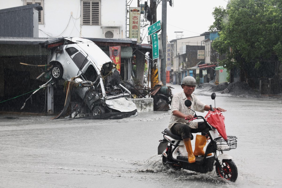  A Guangfu village resident rides his scooter past a damaged car, swept away by floodwaters, in Hualien on September 24, 2025, following the bursting of a barrier lake during the passing of Super Typhoon Ragasa. The typhoon's passage in Taiwan killed at least 15 and injured 18 when a decades-old lake barrier burst in the eastern Hualien county under the storm's heavy rains, according to regional officials. (Photo by I-Hwa Cheng / AFP) ( AFP)