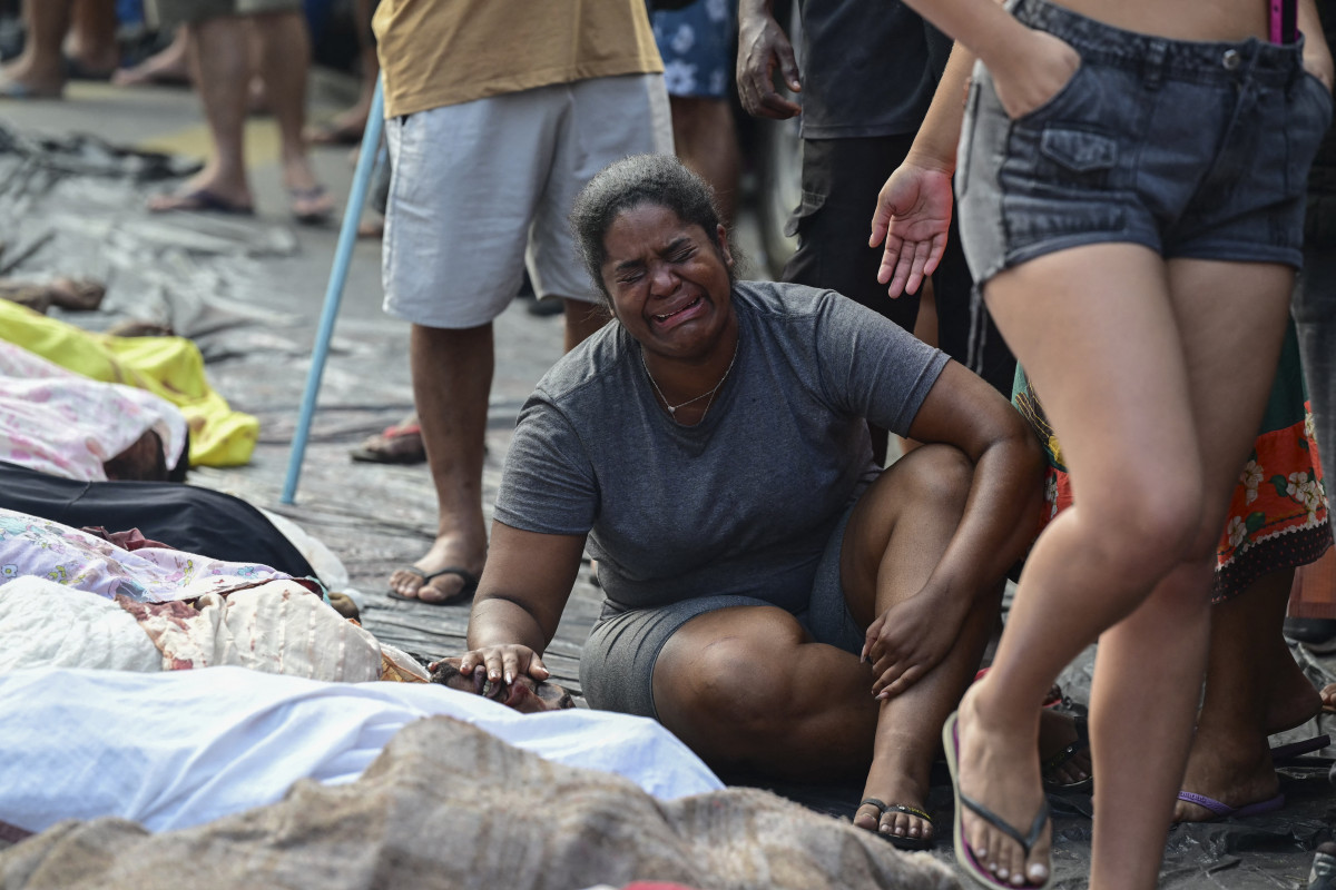 Conteúdo gráfico / Uma mulher chora ao lado de um homem morto, em meio a uma fileira de corpos, na Praça São Lucas, na favela Vila Cruzeiro, no Complexo da Penha, Rio de Janeiro, Brasil, em 29 de outubro de 2025, após a Operação Contenção. (Foto de Pablo Porciúncula / AFP) ( AFP)