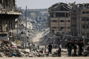 Palestinos caminham perto de uma área onde militantes do Hamas e membros do Comitê Internacional da Cruz Vermelha (CICV) (ao fundo) procuram os corpos de reféns israelenses nos escombros da Cidade de Gaza, em 3 de novembro de 2025. O cessar-fogo de 10 de outubro, que encerrou a guerra entre Israel e Hamas, já durava dois anos e foi mediado pelo presidente dos EUA, Donald Trump, foi duramente testado pelos contínuos ataques israelenses e pelas alegações de ataques palestinos contra soldados israelenses. Desde o início da trégua, o Hamas libertou os 20 reféns sobreviventes e começou a entregar os restos mortais de 28 prisioneiros falecidos. (Foto de Omar AL-QATTAA / AFP)