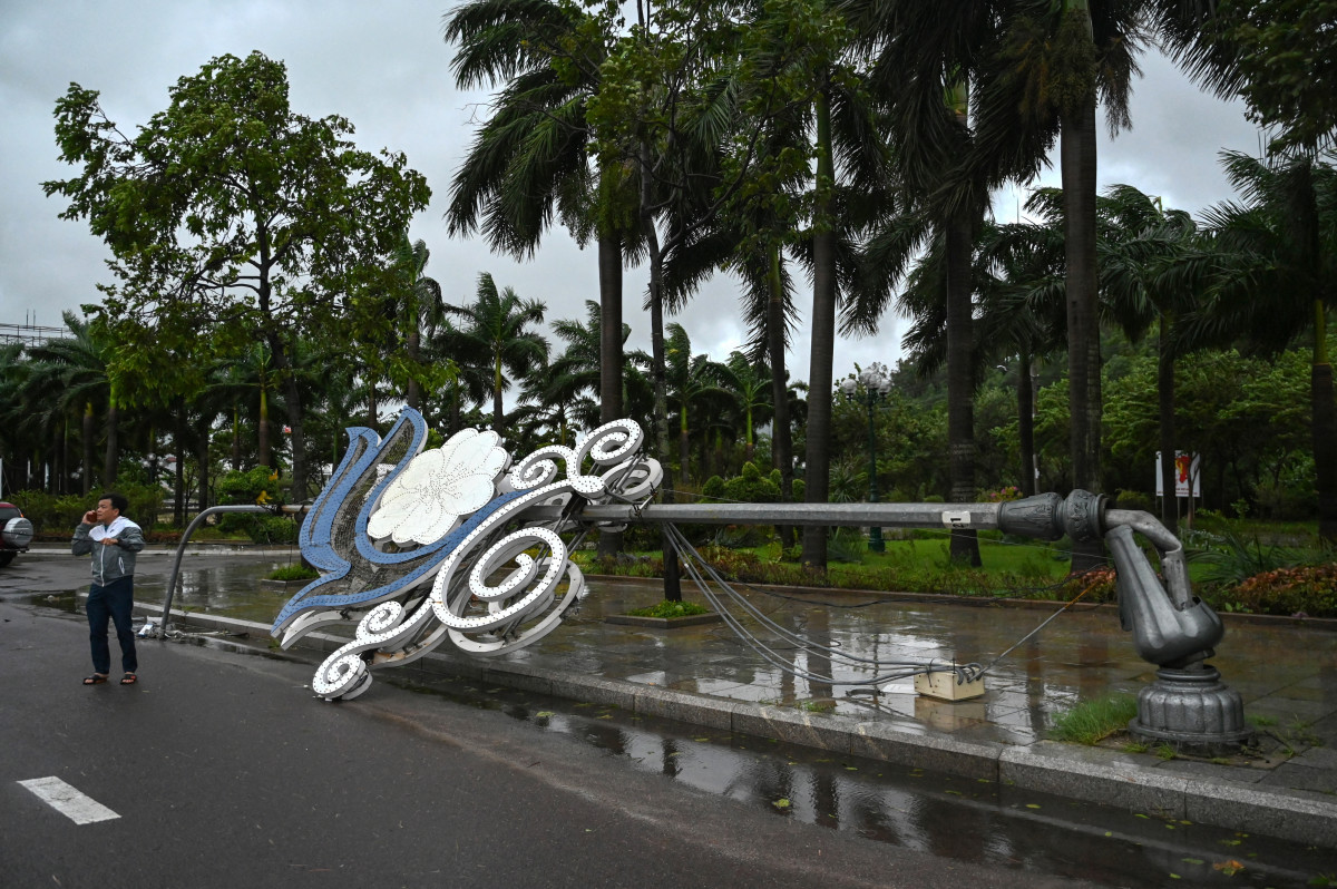 Um homem fala ao telefone ao lado de um poste de luz que desabou devido aos fortes ventos antes da chegada do tufão Kalmaegi, perto da praia de Quy Nhon, na província de Gia Lai, no centro do Vietnã, em 6 de novembro de 2025. A velocidade dos ventos do tufão Kalmaegi aumentava em 6 de novembro, enquanto ele se dirigia para o Vietnã, onde crescia o temor de que o tufão pudesse agravar os danos causados ??pelas inundações que já haviam deixado 47 mortos há uma semana. (Foto de NHAC NGUYEN / AFP)/ AFP