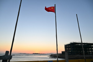 A bandeira chinesa &eacute; vista ao p&ocirc;r do sol na ilha de Pingtan, o ponto mais pr&oacute;ximo de Taiwan, na prov&iacute;ncia de Fujian, no leste da China, em 29 de dezembro de 2025. A China lan&ccedil;ou exerc&iacute;cios com muni&ccedil;&atilde;o real ao redor de Taiwan em 29 de dezembro, que, segundo ela, simulariam um bloqueio dos principais portos da ilha autogovernada, levando Taipei a condenar a "intimida&ccedil;&atilde;o militar" de Pequim. (Foto de ADEK BERRY / AFP)