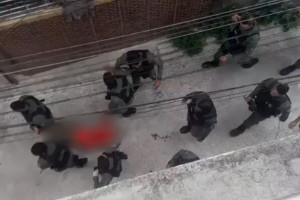 Policiais carregam o corpo de homem baleado.