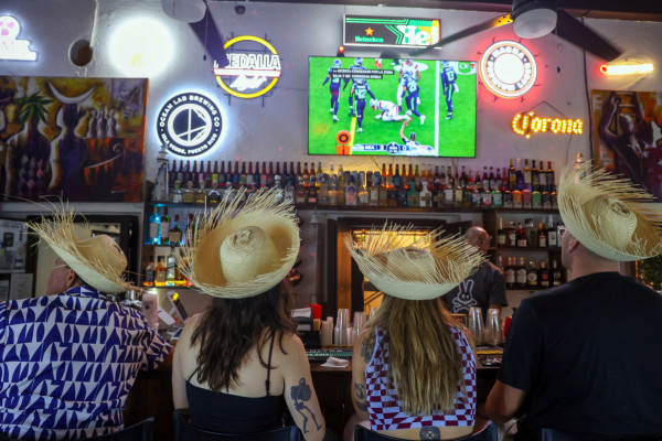 Pessoas usando o tradicional chapéu porto-riquenho "pava" assistem ao Super Bowl LX enquanto aguardam o show do intervalo com Bad Bunny (Jaydee Lee SERRANO/AFP)