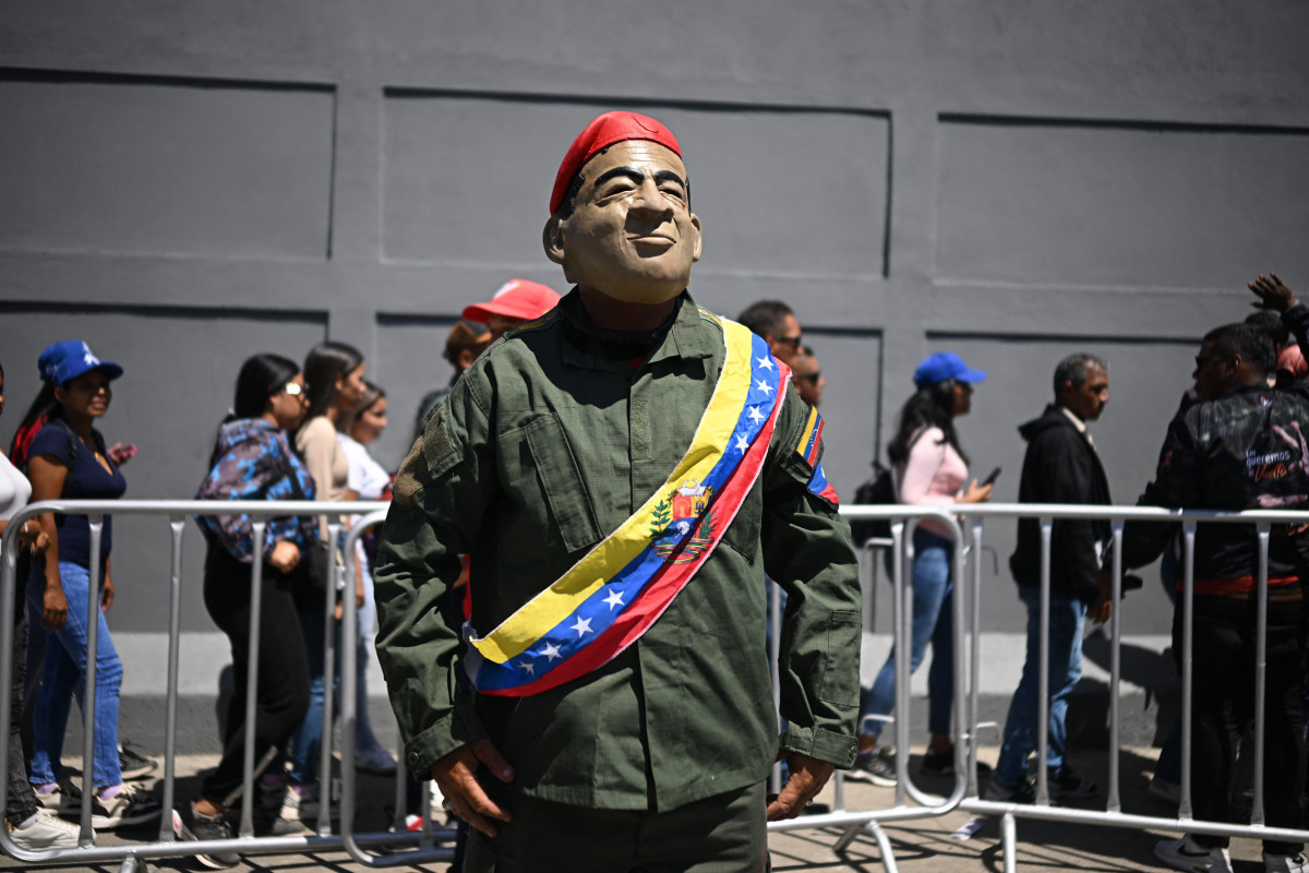 Um homem usando uma máscara do falecido presidente Hugo Chávez e vestido com uniforme militar posa durante marcha no Dia Internacional da Juventude, em Caracas./Federico Parra/AFP