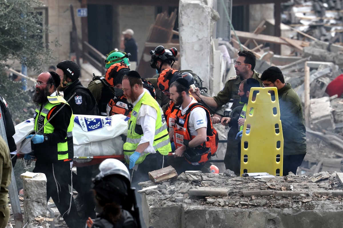 Agentes do serviço de emergência israelense removem corpo do local de um ataque com mísseis em Bet Shemesh/AHMAD GHARABLI / AFP