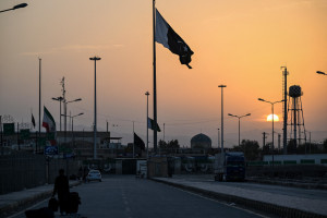 Uma bandeira nacional iraniana (E) tremula a meio mastro enquanto a bandeira do Paquist&atilde;o (C) ondula ao p&ocirc;r do sol na passagem de fronteira entre o Paquist&atilde;o e o Ir&atilde; em Taftan, prov&iacute;ncia do Baluchist&atilde;o, em 4 de mar&ccedil;o de 2026. Foto de Banaras KHAN / AFP)