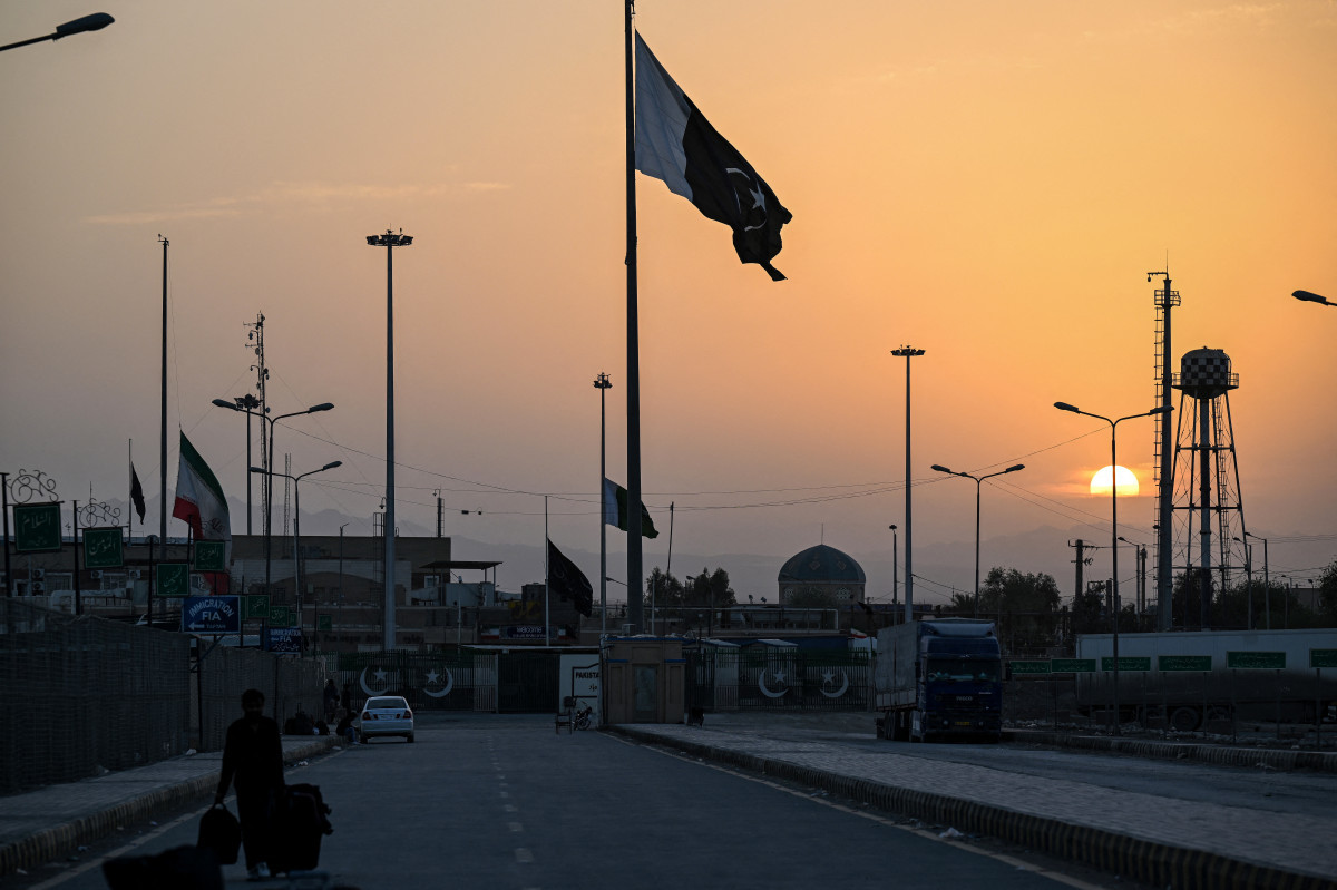Uma bandeira nacional iraniana (E) tremula a meio mastro enquanto a bandeira do Paquistão (C) ondula ao pôr do sol na passagem de fronteira entre o Paquistão e o Irã em Taftan, província do Baluchistão, em 4 de março de 2026. Foto de Banaras KHAN / AFP)/ AFP