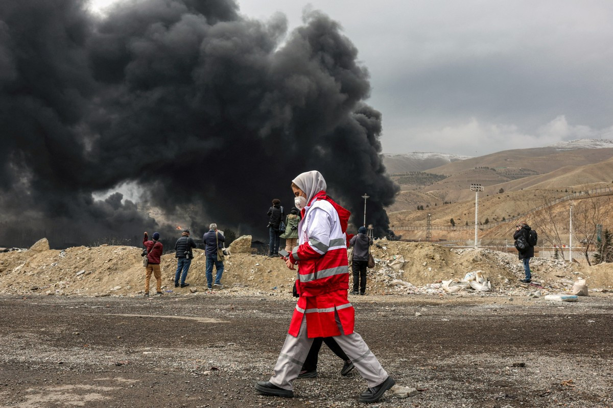 Integrantes do Crescente Vermelho do Irã caminham perto de fumaça após um ataque aéreo à refinaria de petróleo de Shahran, em Teerã/ AFP