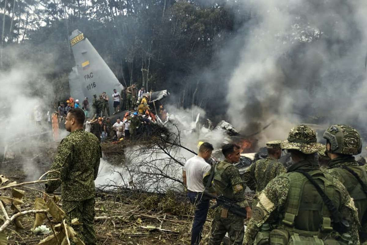 Soldados e equipes de resgate perto de um Hércules da Força Aérea soltando densa fumaça após a aeronave ter caído durante a decolagem em Puerto Leguizamo, Colômbia/Foto por DANIEL ORTIZ/AFP
