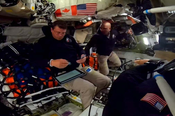 Esta captura de tela de uma transmissão ao vivo da NASA mostra o astronauta da NASA e comandante da Artemis II, Reid Wiseman (à esquerda), e o astronauta da NASA e piloto da Artemis II, Victor Glover, trabalhando dentro da espaçonave Orion enquanto ultrapassam o ponto intermediário entre a Terra e a Lua. ( AFP)