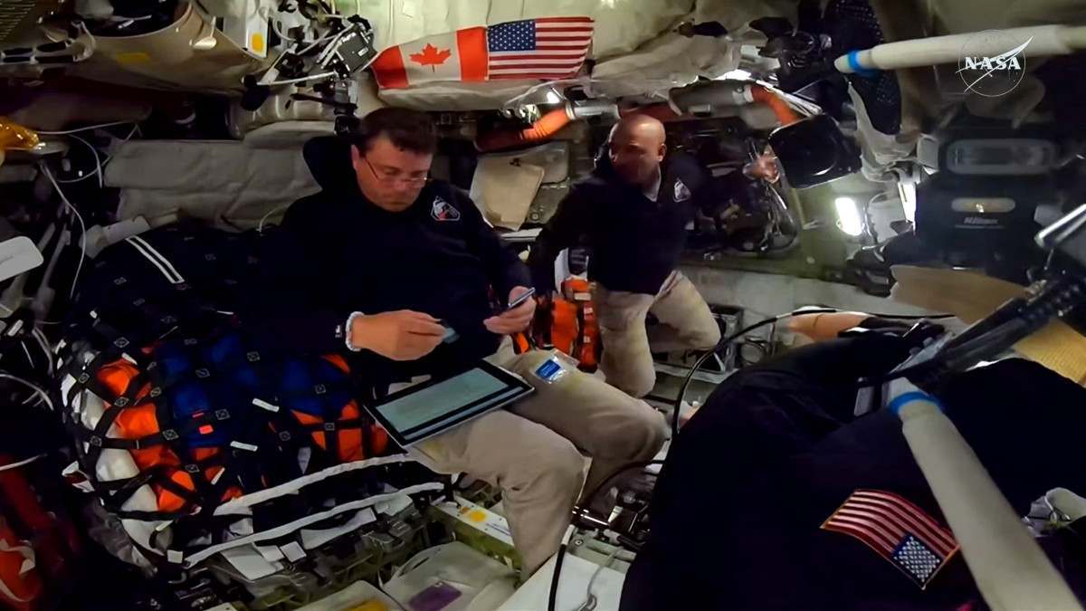 Esta captura de tela de uma transmissão ao vivo da NASA mostra o astronauta da NASA e comandante da Artemis II, Reid Wiseman (à esquerda), e o astronauta da NASA e piloto da Artemis II, Victor Glover, trabalhando dentro da espaçonave Orion enquanto ultrapassam o ponto intermediário entre a Terra e a Lua. ( AFP)