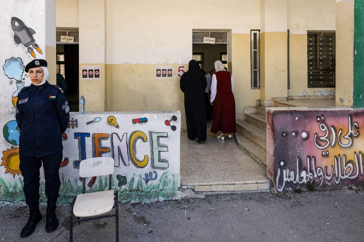 Membro das forças de segurança palestinas guarda a entrada de uma seção eleitoral enquanto os eleitores chegam durante as eleições municipais/JAAFAR ASHTIYEH/AFP