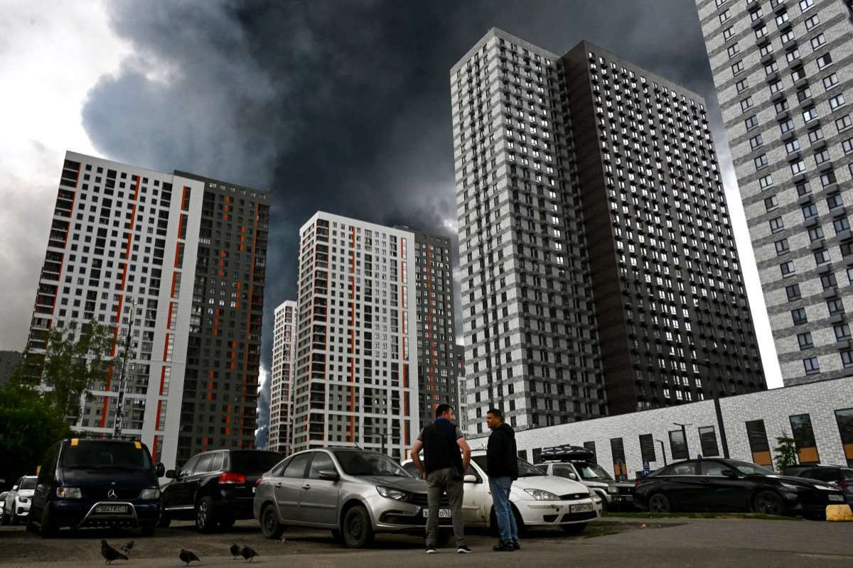 Homens interagem em uma área residencial tomada por fumaça preta em Moscou, em 18 de junho de 2026. / AFP