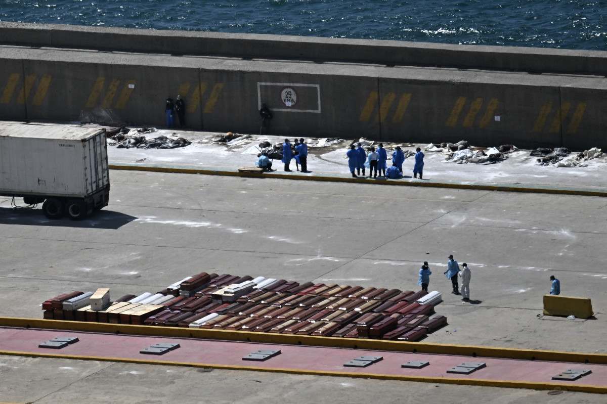 Peritos forenses estão ao lado de vítimas e caixões no porto de La Guaira, na Venezuela/Juan Barreto/AFP