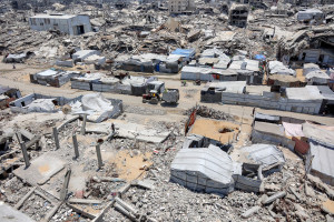 Barracas e abrigos aparecem ao lado de escombros de pr&eacute;dios desabados na cidade de Gaza