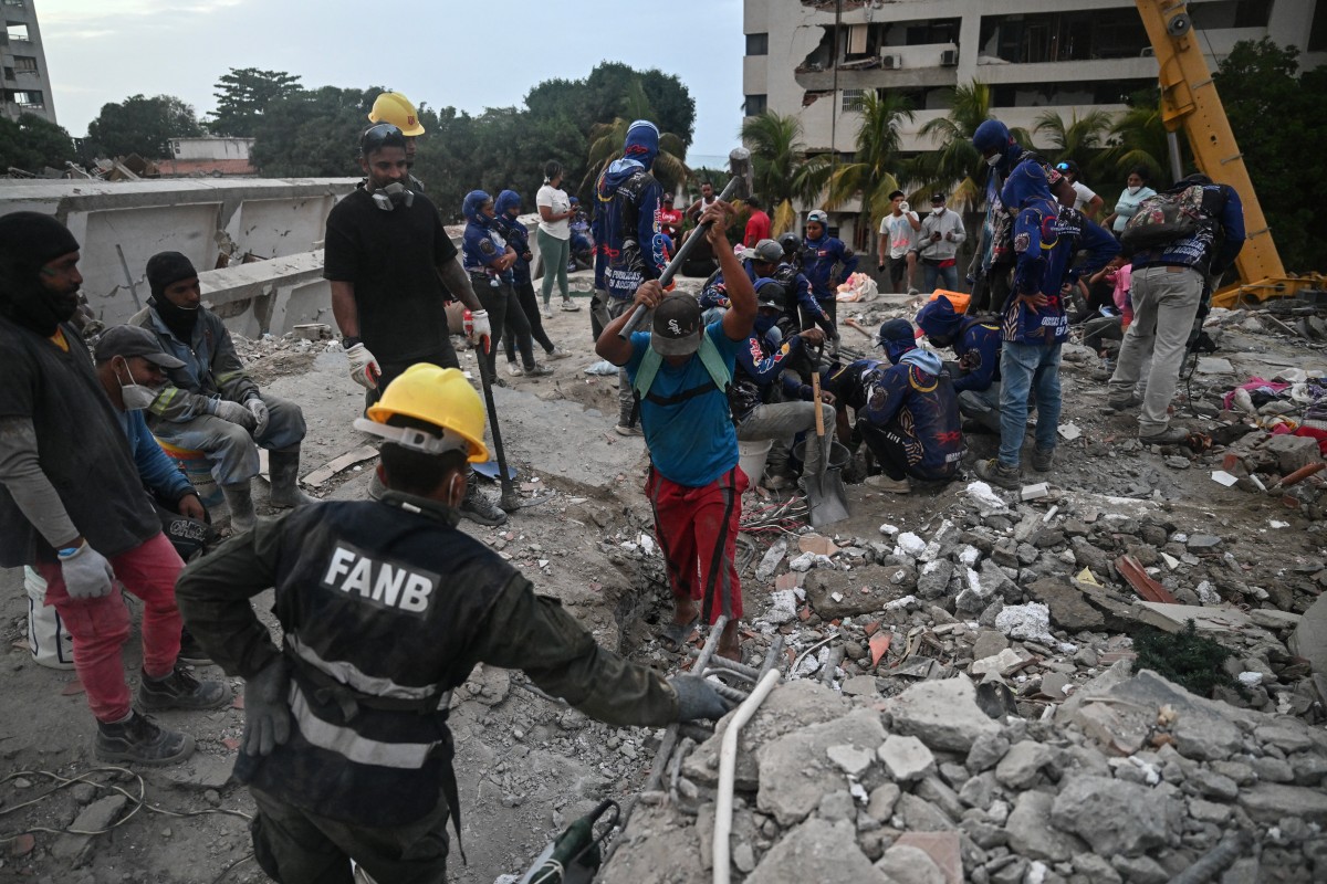 Voluntários e equipes de resgate buscam corpos entre os escombros de edifícios danificados pelos terremotos de 24 de junho em Tanaguarena, no estado de La Guaira, Venezuela/ AFP