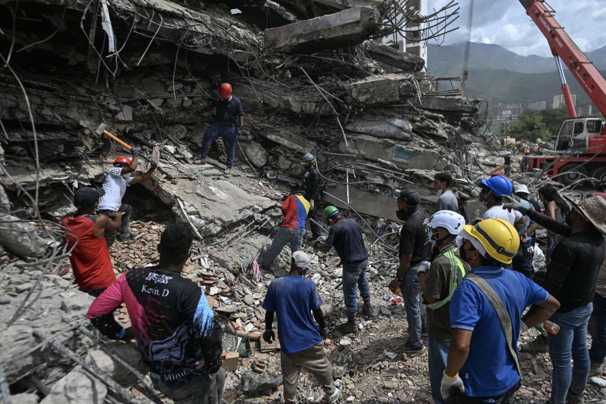 Voluntários e equipes de resgate buscam corpos entre os escombros de um prédio que desabou em Caraballeda, na Venezuela, em 23 de julho de 2026, quase um mês após os terremotos de 24 de junho/JUAN BARRETO/AFP