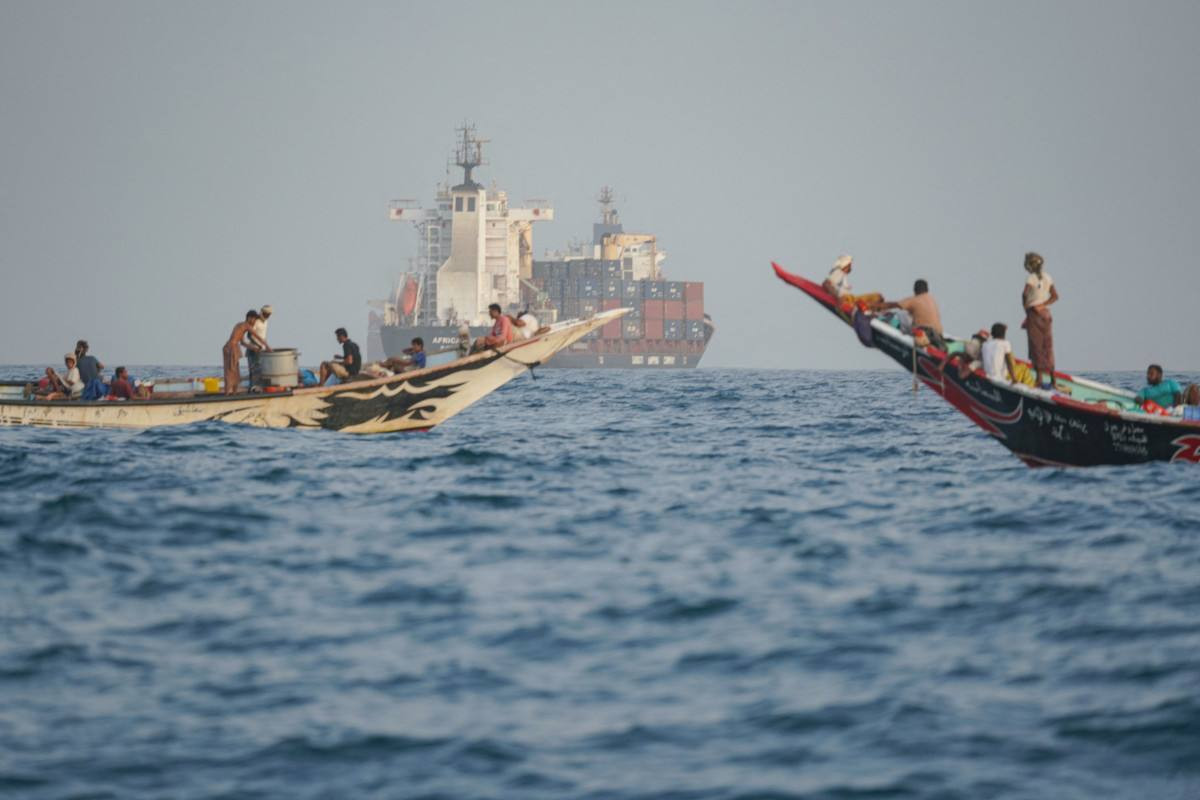 Pessoas navegam próximo a porta-contêineres ancorados perto do Estreito de Bab el-Mandeb, na costa do Iêmen, no Golfo de Aden/ AFP