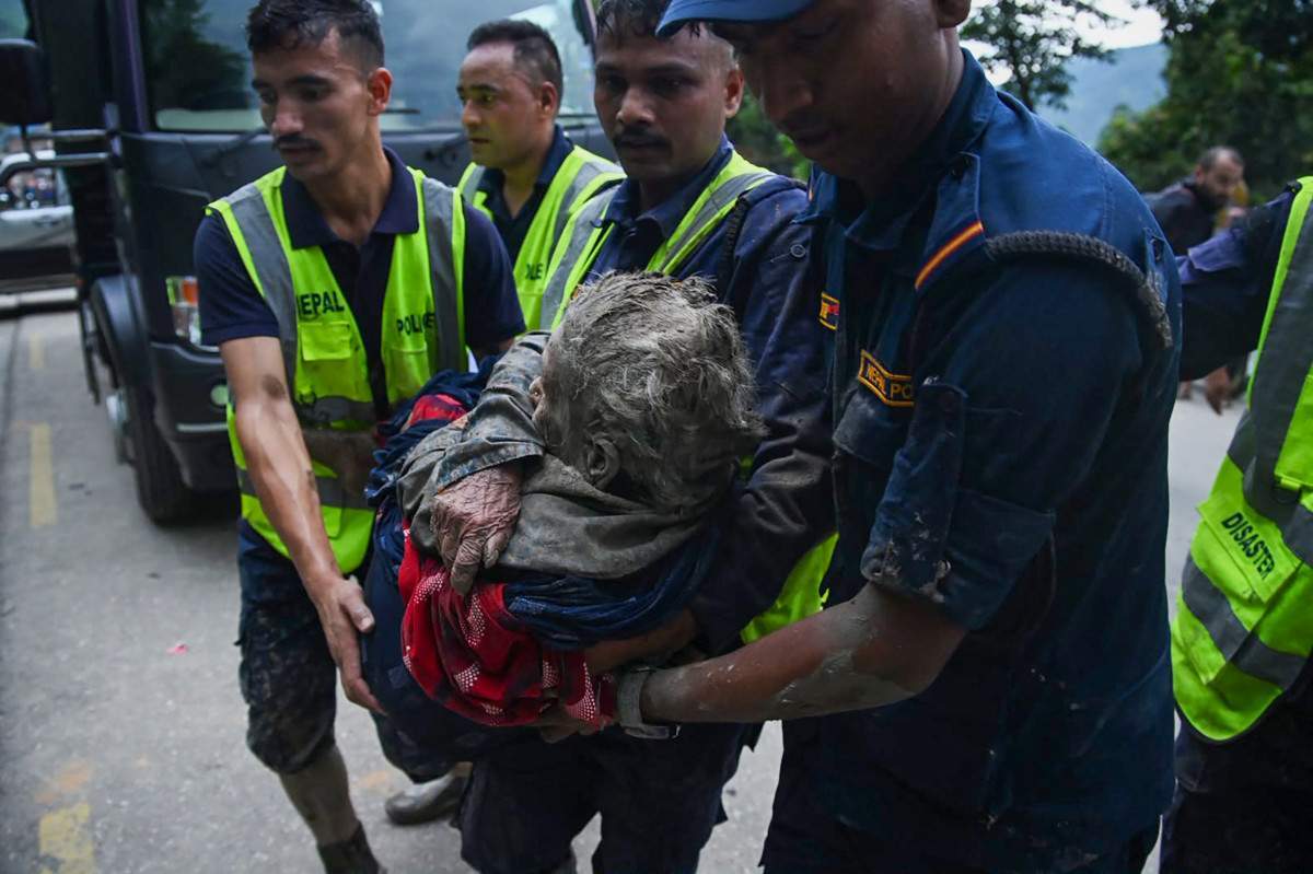 Equipes de resgate carregando uma mulher afetada pelas enchentes/PRAKASH MATHEMA / AFP