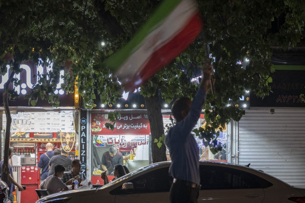 Manifestante iraniano hasteia bandeira do país em rua de Teerã/ NurPhoto via AFP