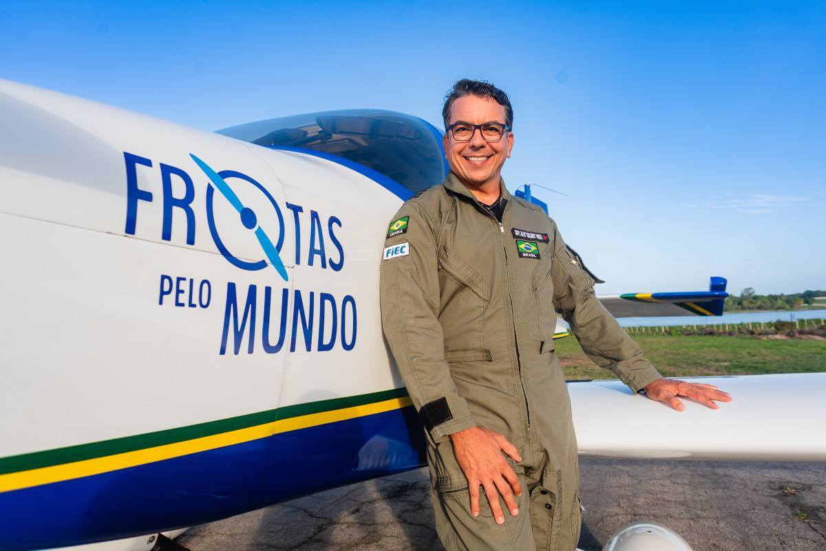 Piloto vestindo um uniforme na lateral da aeronave, tocando no avi&atilde;o com uma m&atilde;o e esbanjando um sorriso. /Divulga&ccedil;&atilde;o/Alex Frota. 