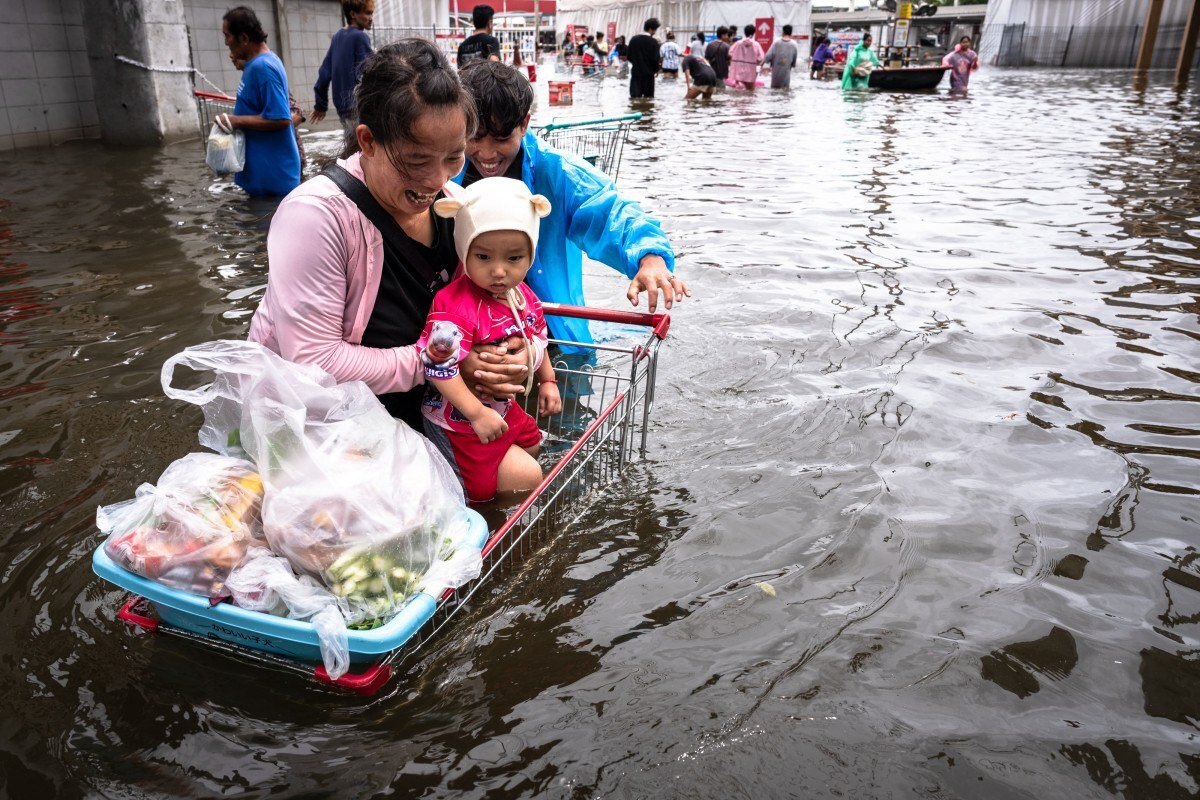 Pessoas caminham por águas de enchente após fazerem compras no distrito de Bang Kapi, em Bangkok/CHANAKARN LAOSARAKHAM/AFP