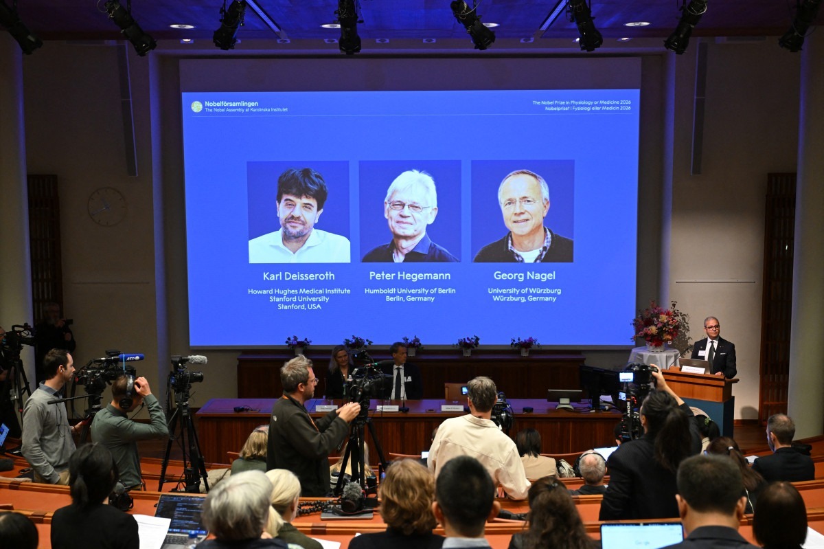 Abdel El Manira, professor de neurociência do Instituto Karolinska, fala diante de uma tela que exibe retratos do cientista americano Karl Deisseroth e dos cientistas alemães Peter Hegemann e Georg Nagel durante o anúncio dos vencedores do Prêmio Nobel de Fisiologia ou Medicina de 2026/JONATHAN NACKSTRAND/AFP