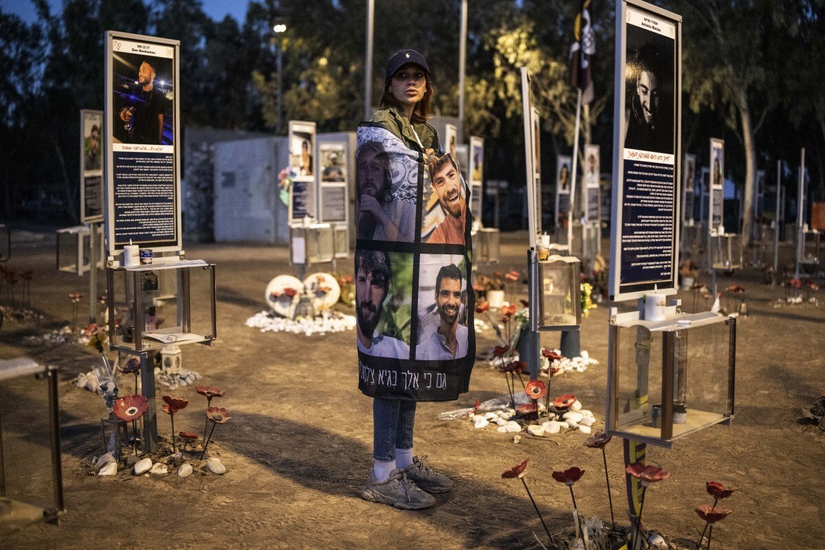 Uma pessoa enlutada segura um cartaz com retratos de vítimas enquanto está no local do festival de música Nova, em Israel/JOHN WESSELS/AFP